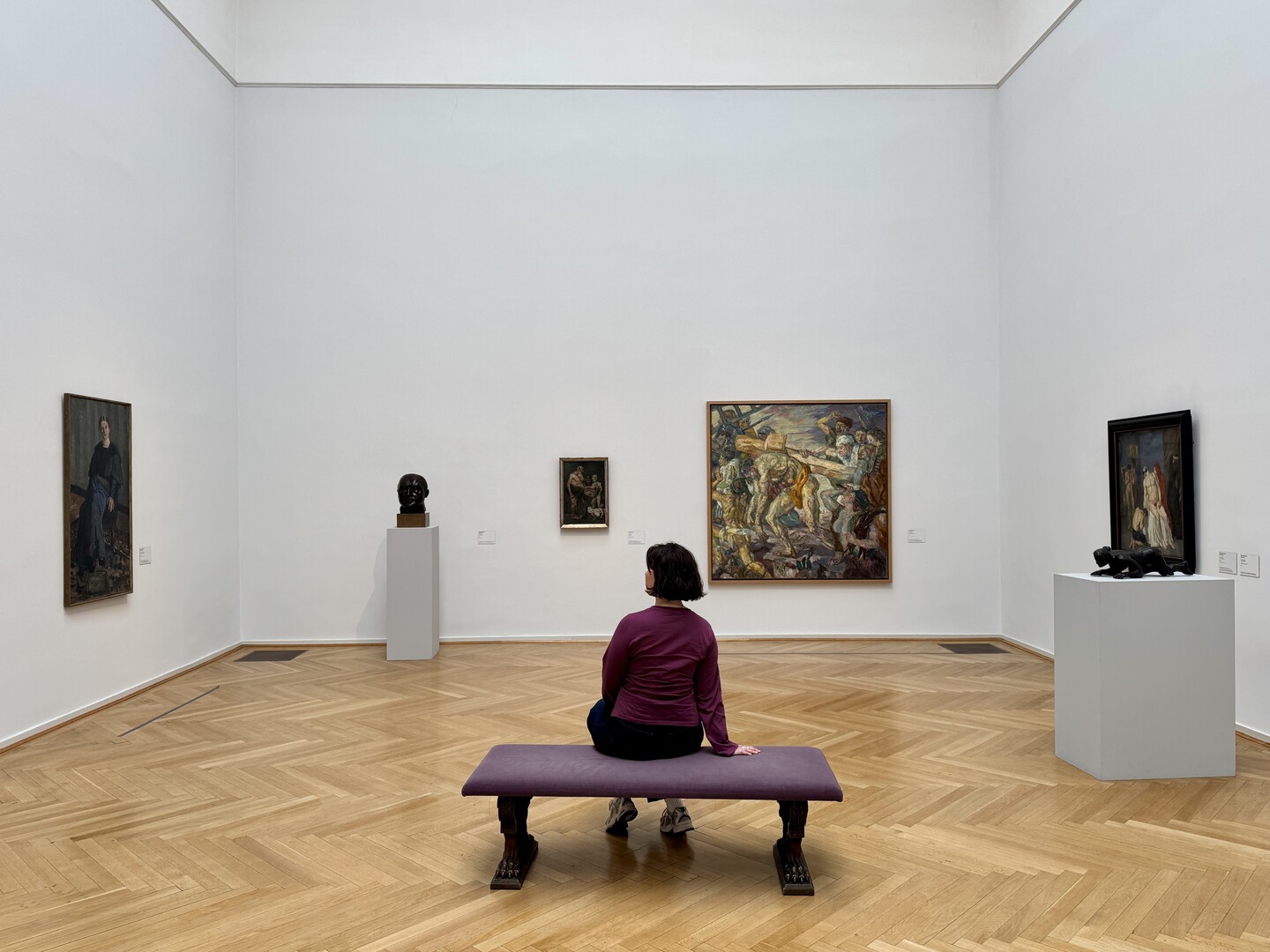 Person sitzt auf Bank in hellem Galerieraum mit Kunstwerken von Max Beckmann
