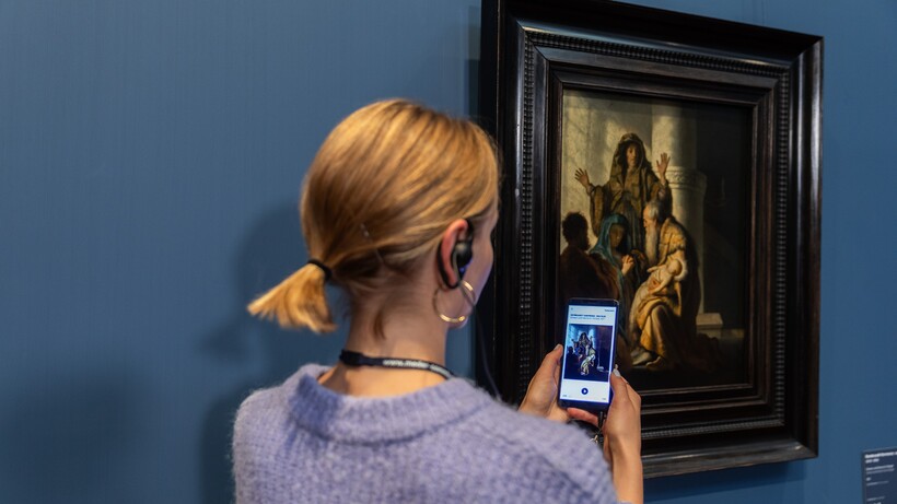 Eine Frau mit Handy und Kopfhörern vor dem Gemälde von Rembrandt Harmensz. van Rijn (1606–1669)