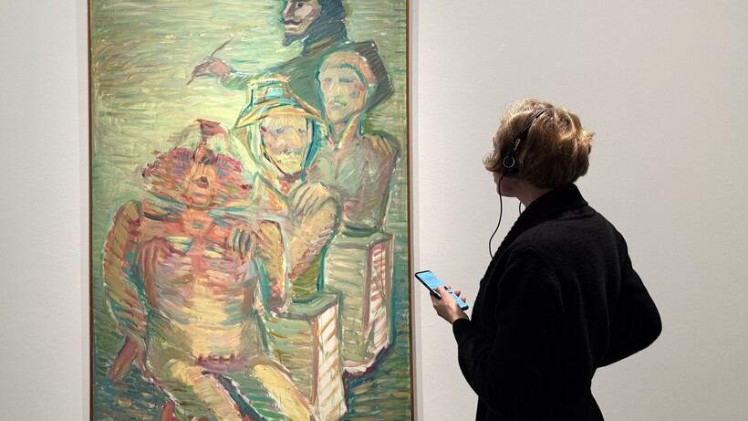 Eine Frau mit Kopfhörern vor dem Werk »Traditionskette« von Maria Lassnig