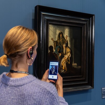 Eine Frau mit Handy und Kopfhörern vor dem Gemälde von Rembrandt Harmensz. van Rijn (1606–1669)
